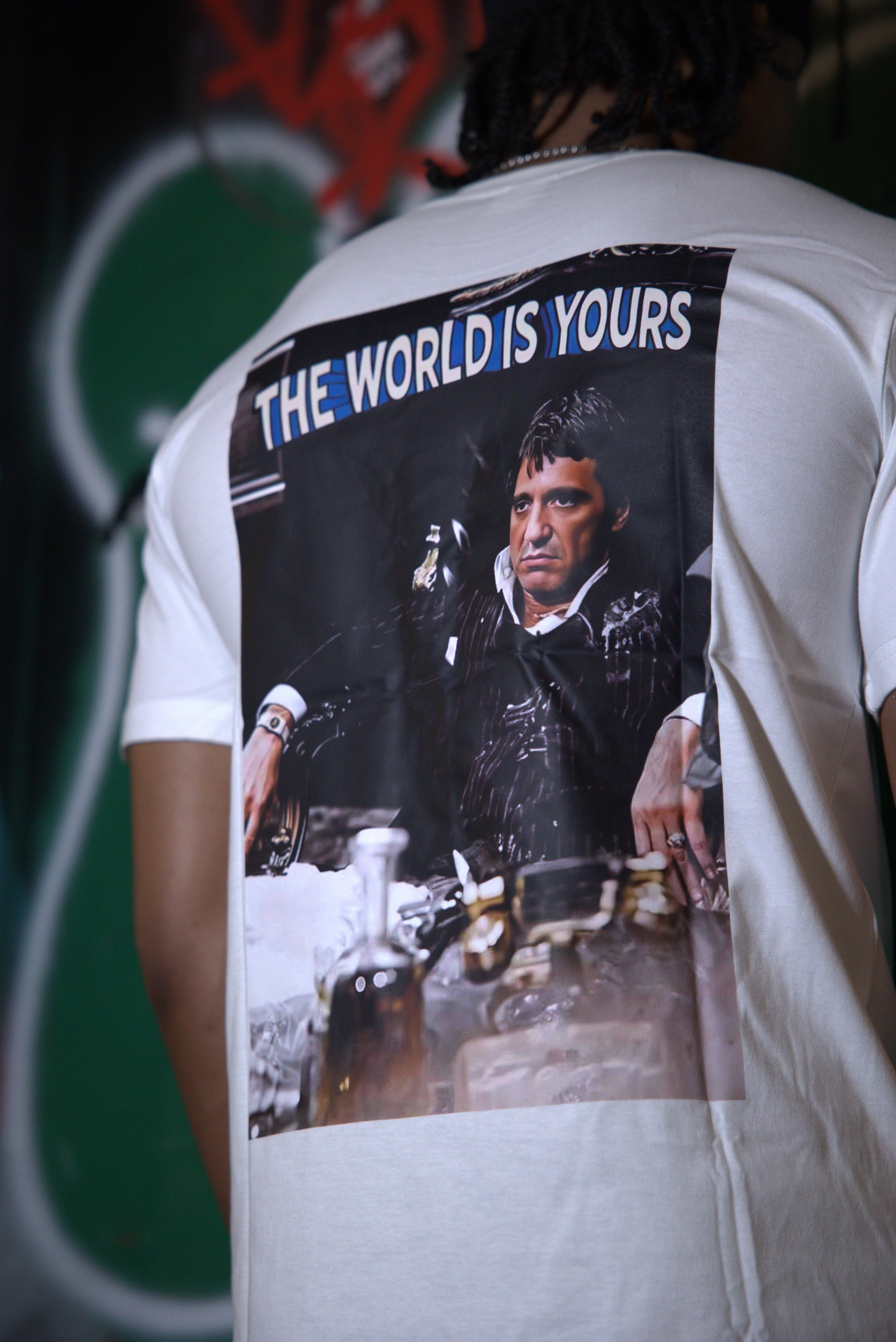 White t-shirt with a graphic design of a person and 'The World is Yours' text, worn by a person.
